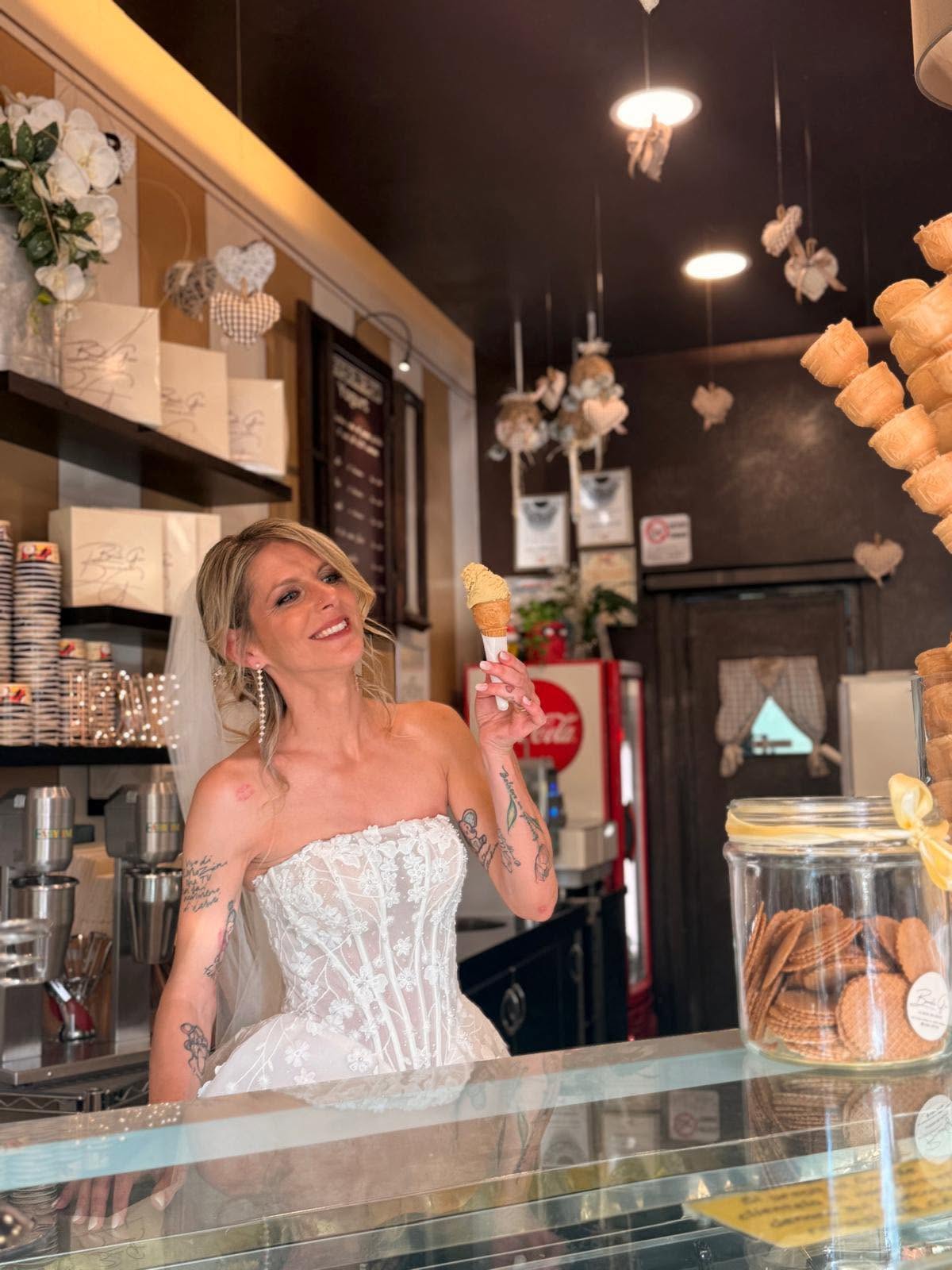 Gioia dietro il banco della gelateria, in abito da sposa, con un cono di gelato in mano